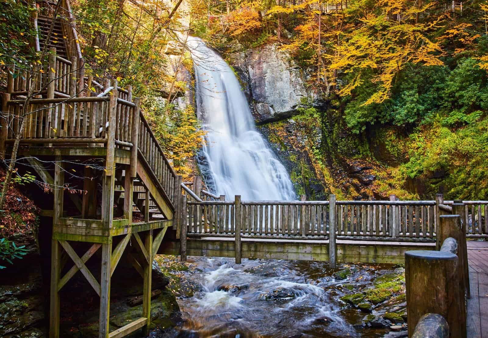 Serene waterfall in a lush autumn forest with a wooden observation deck for nature lovers and adventure seekers.