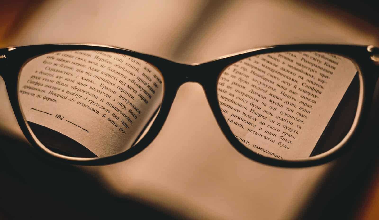Close-up of reading glasses reflecting an open book, emphasizing travel and adventure reading materials.