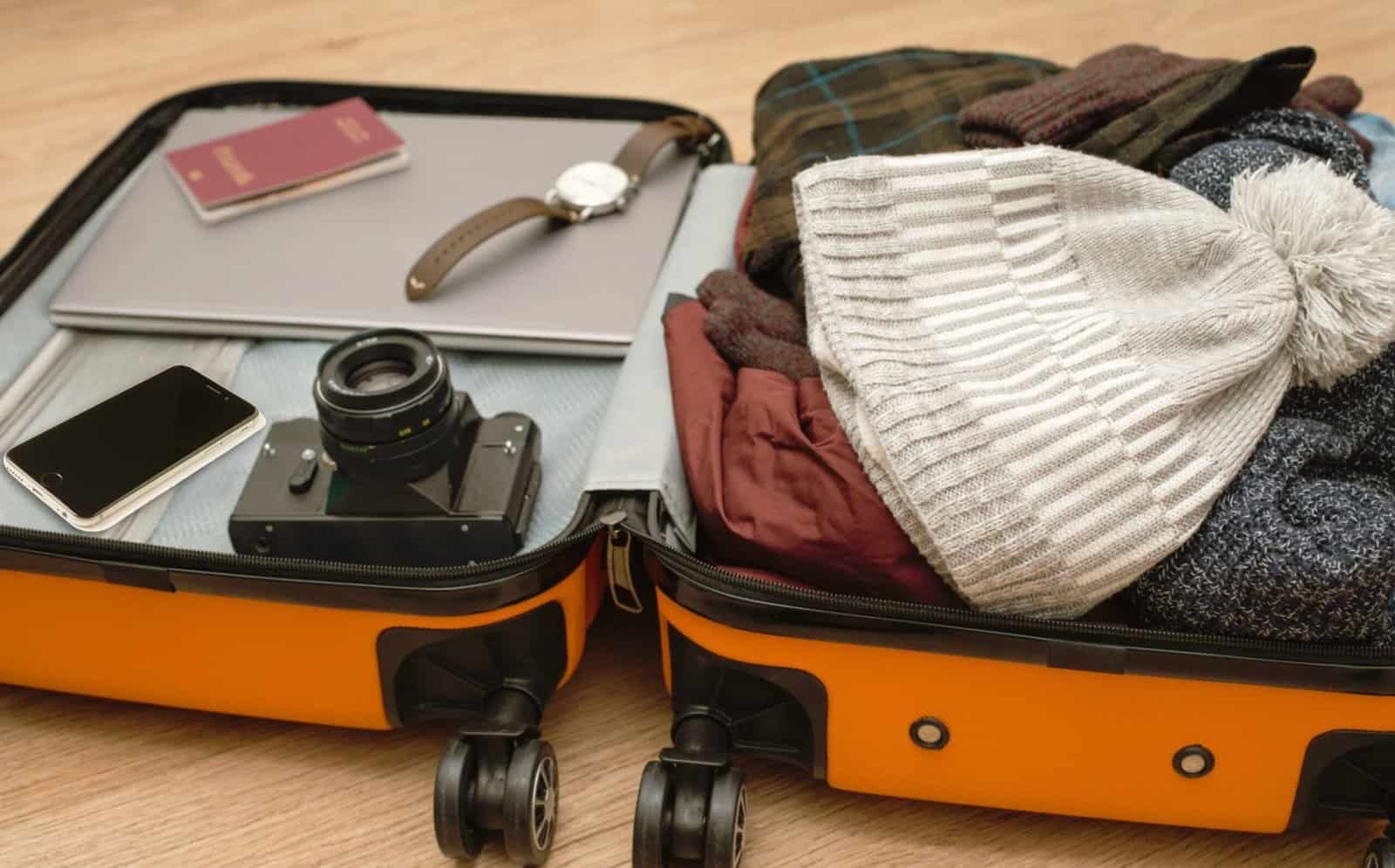 Open suitcase filled with winter clothing, accessories, and travel essentials for a winter getaway.