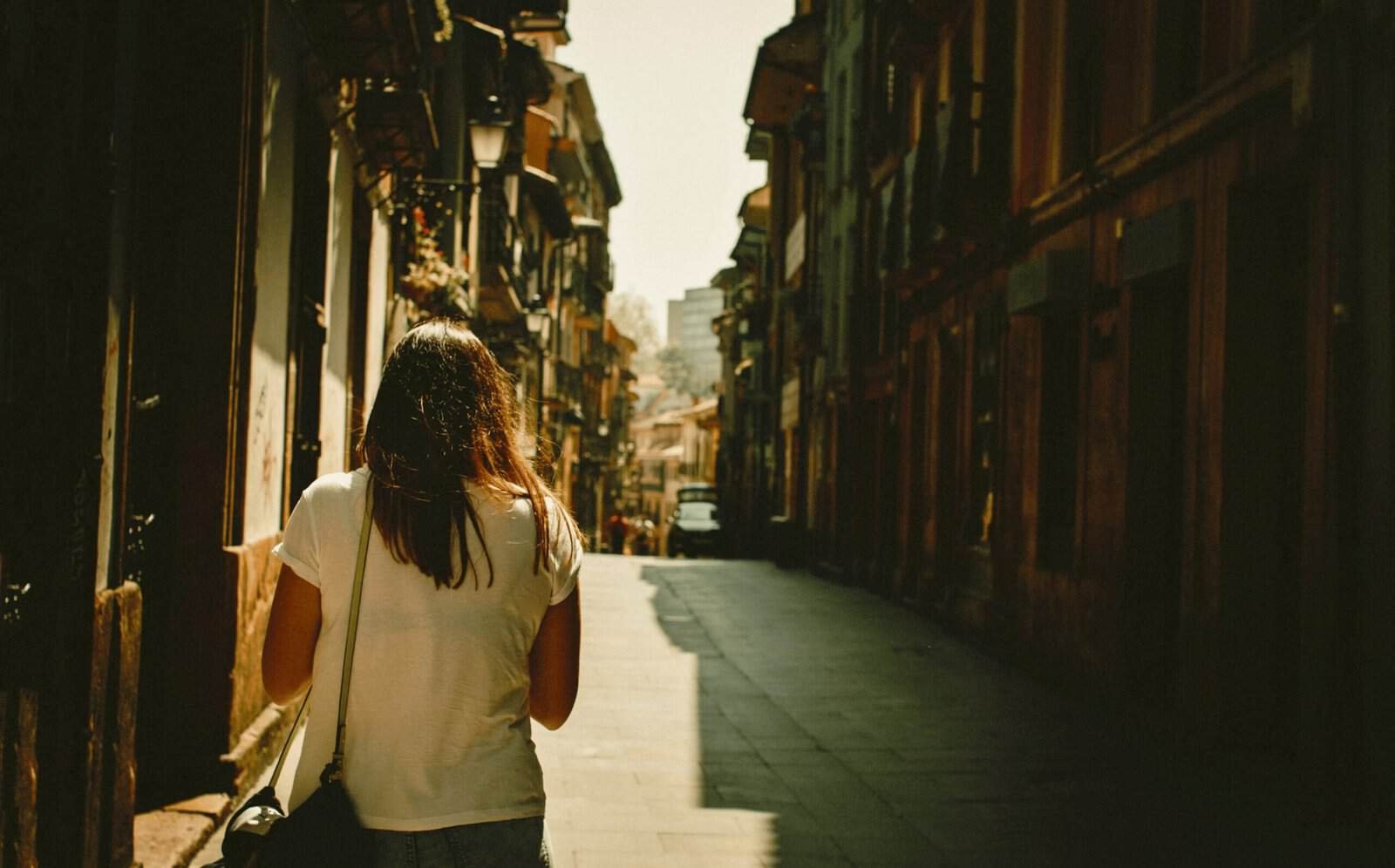 A woman walking down a quiet, sunlit city street with colorful buildings on either side, capturing the essence of slow travel and urban exploration.